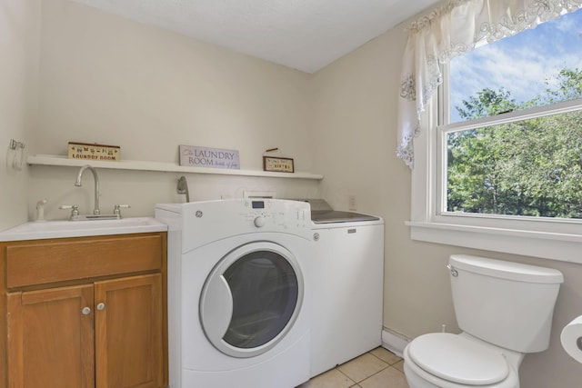 clothes washing area with light tile patterned flooring, washer and clothes dryer, laundry area, and a sink