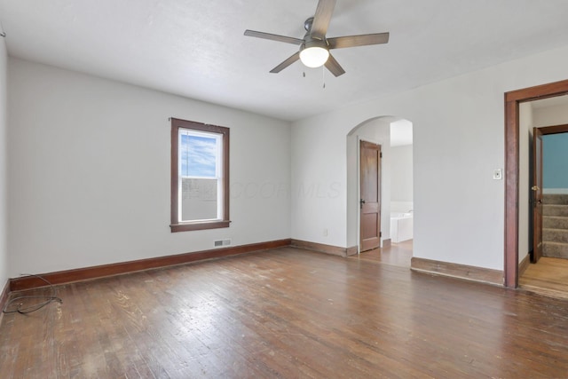 empty room with visible vents, baseboards, ceiling fan, arched walkways, and wood-type flooring