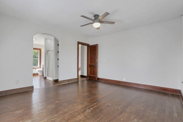 spare room featuring arched walkways, baseboards, a ceiling fan, and wood-type flooring