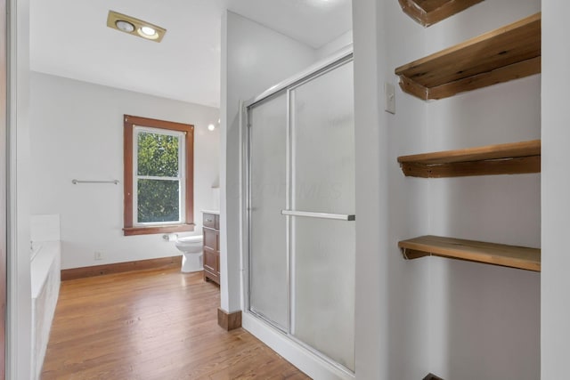 bathroom featuring wood finished floors, toilet, baseboards, and a shower stall
