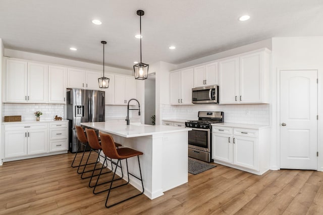 kitchen with light countertops, a sink, a kitchen breakfast bar, stainless steel appliances, and light wood-style floors