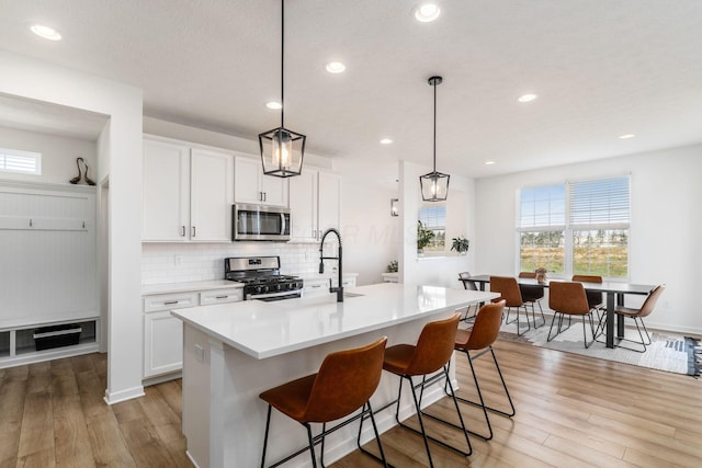 kitchen featuring decorative backsplash, white cabinets, light wood-style flooring, and appliances with stainless steel finishes