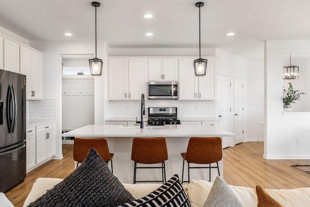 kitchen with light countertops, white cabinets, appliances with stainless steel finishes, a sink, and light wood-type flooring
