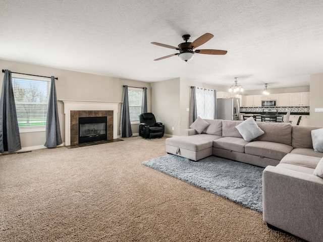 carpeted living area featuring a wealth of natural light, a tile fireplace, ceiling fan with notable chandelier, and baseboards