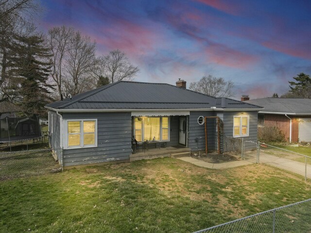 ranch-style home with a front yard, a trampoline, a chimney, fence, and metal roof