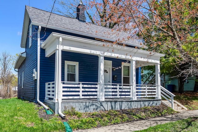 view of front of home with roof with shingles, a porch, and a chimney