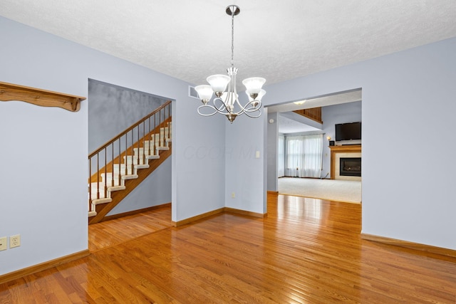 2816 Quail Run Ct, Mansfield, OH 44904 - spare room featuring wood finished floors, stairs, a textured ceiling, a fireplace, and a chandelier