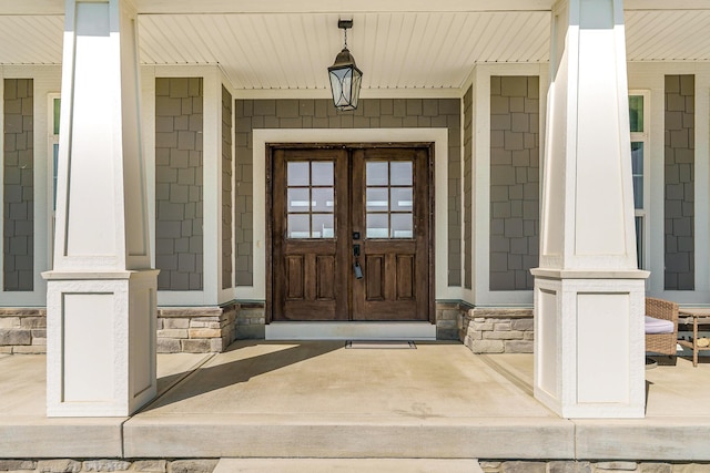 doorway to property with a porch, stone siding, and french doors