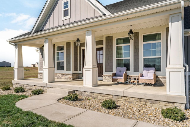 entrance to property featuring stone siding, covered porch, a shingled roof, and board and batten siding
