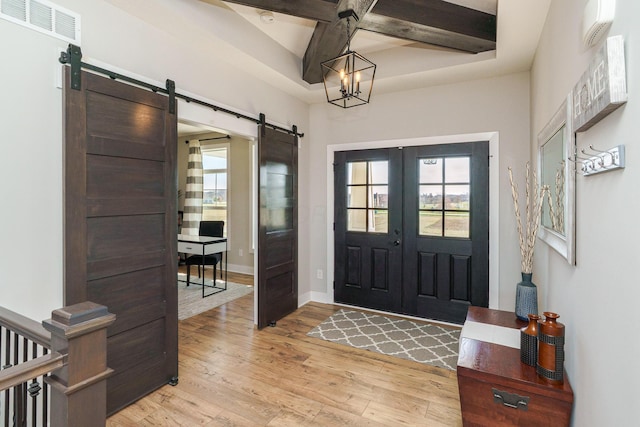 entryway with coffered ceiling, a healthy amount of sunlight, light wood-style floors, a barn door, and visible vents
