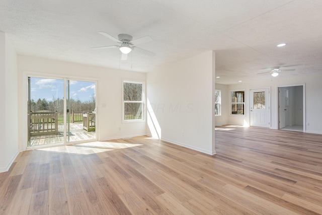 empty room with baseboards, a textured ceiling, ceiling fan, and light wood-type flooring