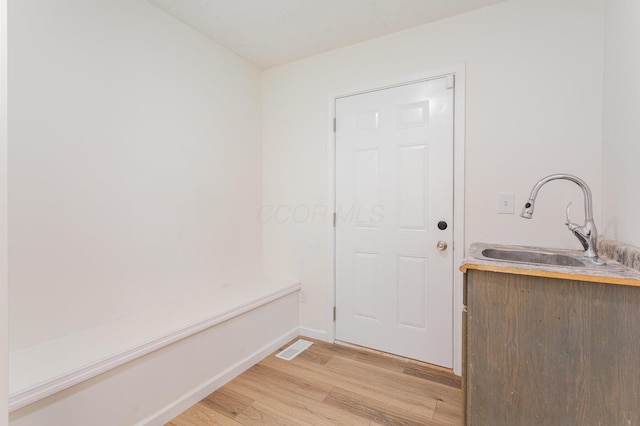 doorway to outside featuring a sink, baseboards, visible vents, and light wood-type flooring