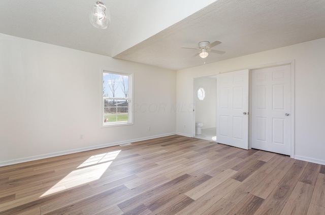 interior space featuring a ceiling fan, baseboards, light wood-style floors, and a textured ceiling