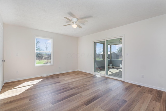 empty room with plenty of natural light, a textured ceiling, light wood finished floors, and ceiling fan