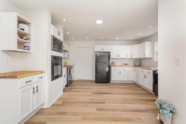 kitchen with white cabinetry, butcher block countertops, black appliances, light wood-style floors, and decorative backsplash