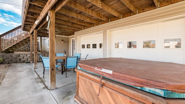 view of patio with driveway, stairs, a garage, outdoor dining area, and a hot tub