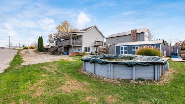 back of property featuring an outdoor structure, a covered pool, stairs, a deck, and a lawn