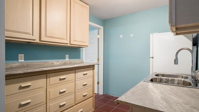 kitchen featuring light countertops, cream cabinetry, dark tile patterned floors, a sink, and freestanding refrigerator