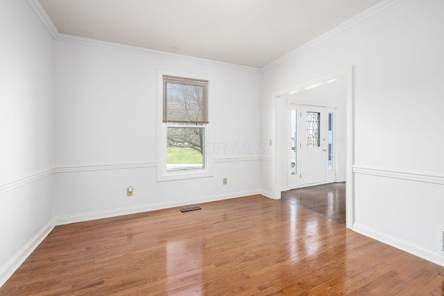 spare room featuring wood finished floors, ornamental molding, baseboards, and visible vents