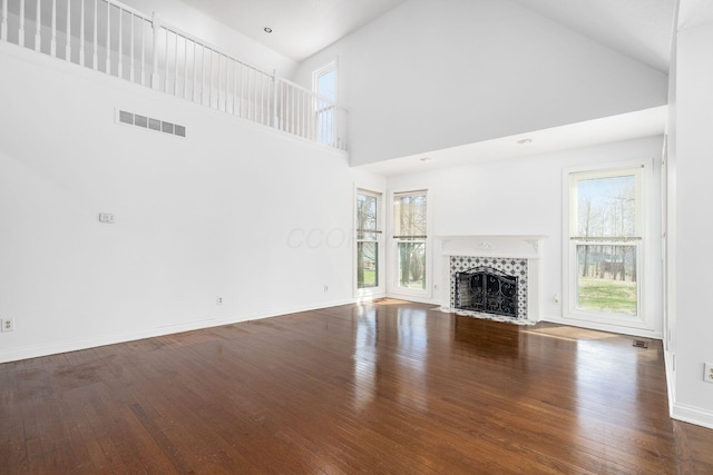 unfurnished living room with hardwood / wood-style floors, baseboards, visible vents, and a tiled fireplace