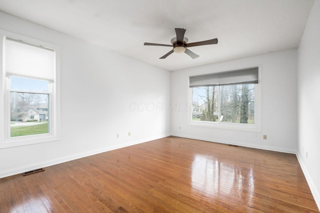 unfurnished room featuring baseboards, visible vents, hardwood / wood-style flooring, and a ceiling fan