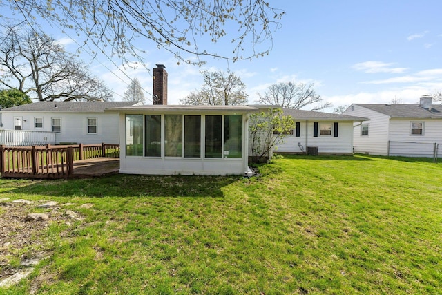 rear view of house featuring a sunroom, a chimney, and a lawn