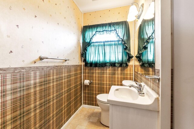half bath with toilet, wallpapered walls, and a wainscoted wall