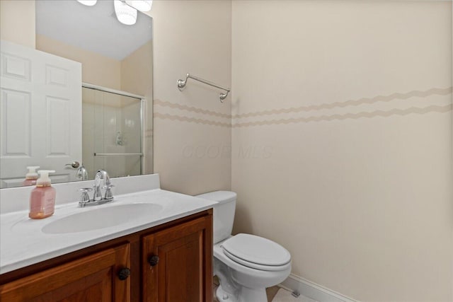 bathroom featuring a shower with door, vanity, baseboards, and toilet