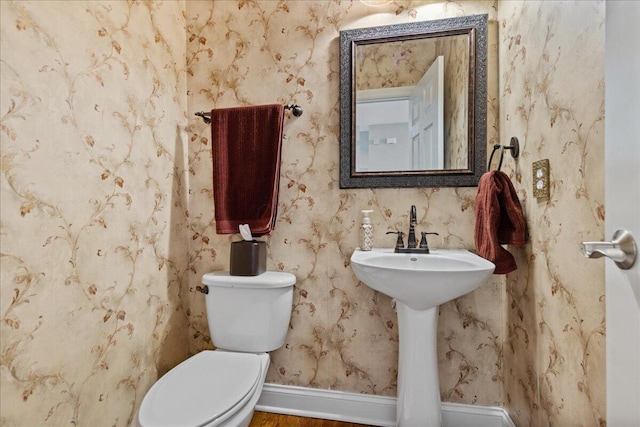 half bathroom with baseboards, wallpapered walls, and toilet