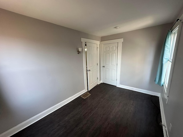 unfurnished bedroom with dark wood-style flooring, baseboards, and visible vents