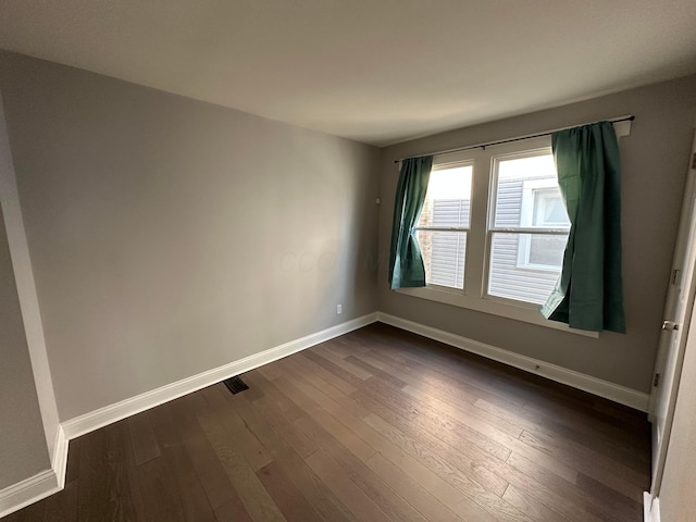spare room featuring dark wood-type flooring and baseboards