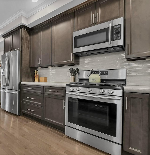 kitchen with crown molding, dark brown cabinets, tasteful backsplash, light wood-style flooring, and appliances with stainless steel finishes
