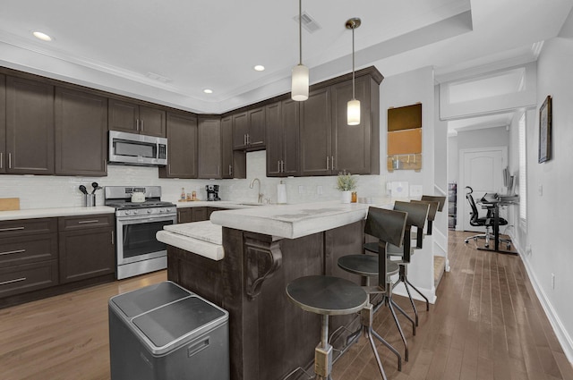 kitchen with dark brown cabinets, a breakfast bar, stainless steel appliances, a peninsula, and visible vents