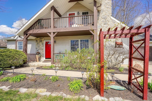 view of front of home with a pergola, stone siding, covered porch, and a balcony