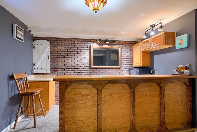 kitchen with brick wall, carpet, a breakfast bar, and a sink