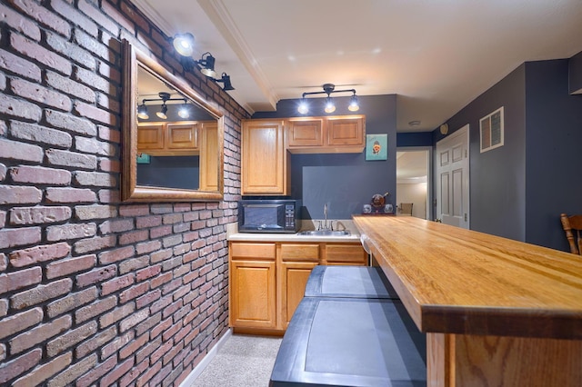 kitchen featuring brick wall, black microwave, a peninsula, visible vents, and a sink