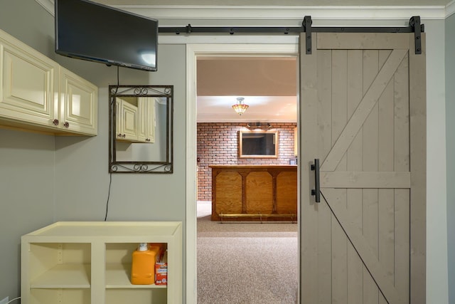 hallway featuring brick wall, a barn door, ornamental molding, and carpet floors