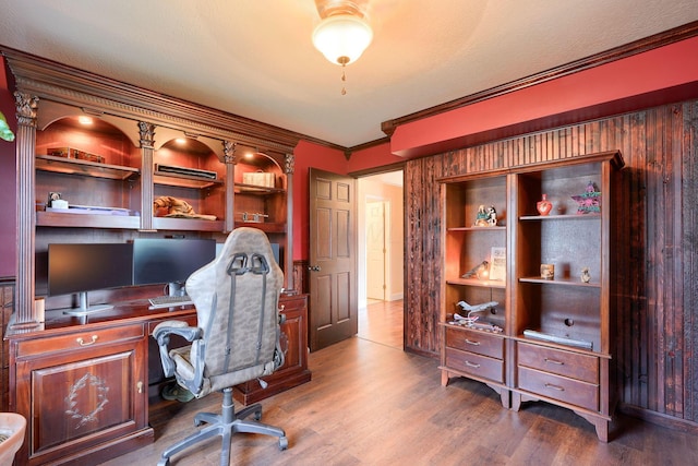 office space with a textured ceiling, built in desk, crown molding, and wood finished floors