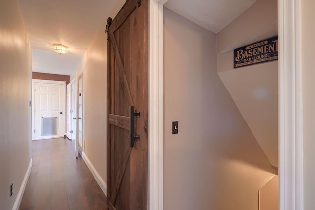 hallway with dark wood-type flooring, baseboards, and a barn door