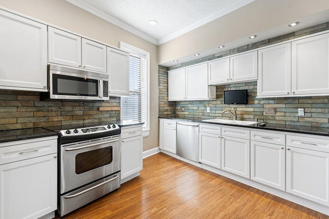kitchen with light wood finished floors, a sink, crown molding, and appliances with stainless steel finishes