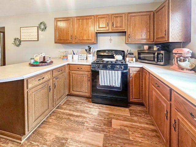 113 Chestnut St SE, Corning, OH 43730 - kitchen with light countertops, stainless steel microwave, light wood-style flooring, a peninsula, and black range with gas stovetop