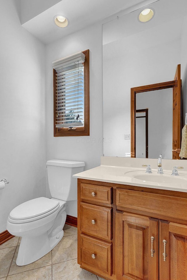 half bathroom featuring toilet, tile patterned floors, vanity, and baseboards