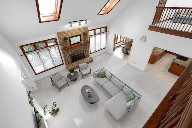 living area featuring baseboards, a brick fireplace, rail lighting, high vaulted ceiling, and a skylight