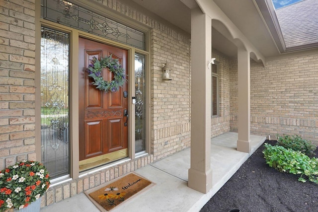 property entrance featuring covered porch, brick siding, and roof with shingles