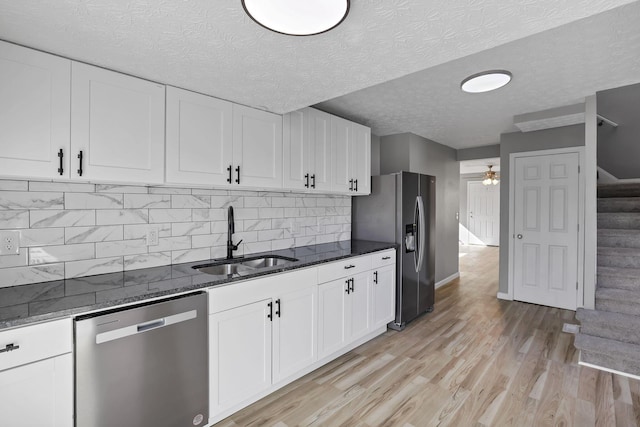 kitchen with dark stone counters, a sink, light wood finished floors, white cabinets, and appliances with stainless steel finishes