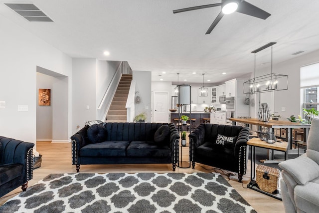 living room featuring stairs, visible vents, light wood-type flooring, and a ceiling fan