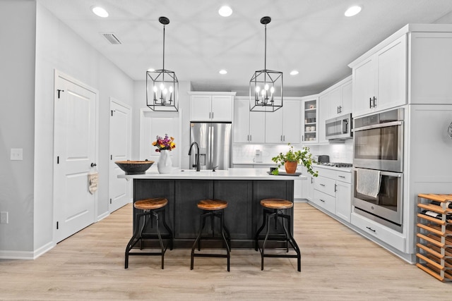 kitchen featuring white cabinets, appliances with stainless steel finishes, light wood-type flooring, an inviting chandelier, and backsplash