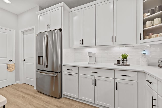 kitchen with white cabinets, light wood-style flooring, stainless steel refrigerator with ice dispenser, and tasteful backsplash