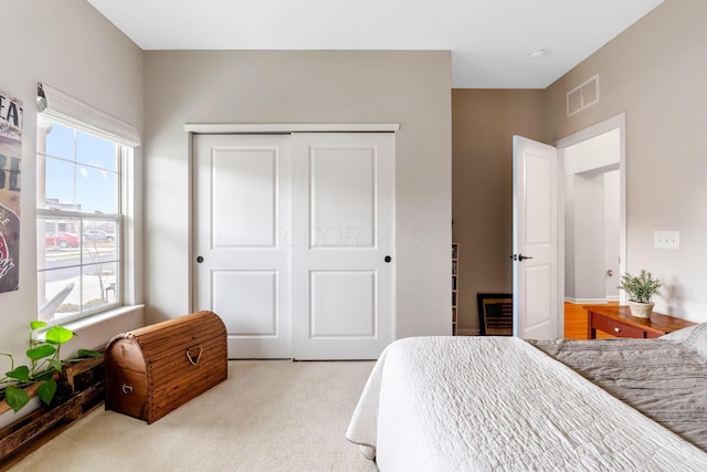 bedroom with a closet, visible vents, and light colored carpet