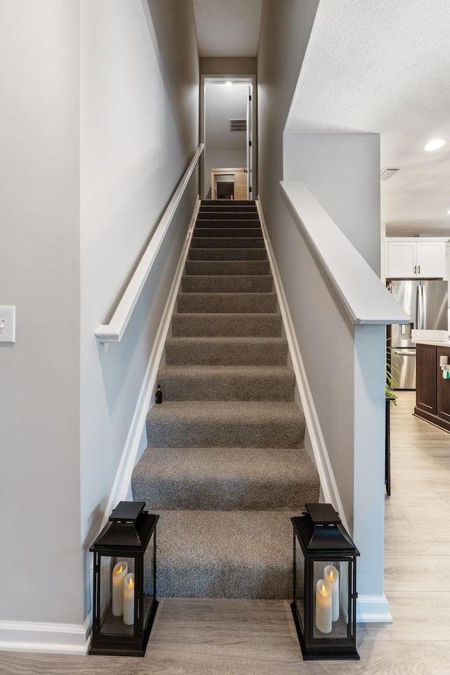 stairway featuring baseboards, visible vents, wood finished floors, and recessed lighting